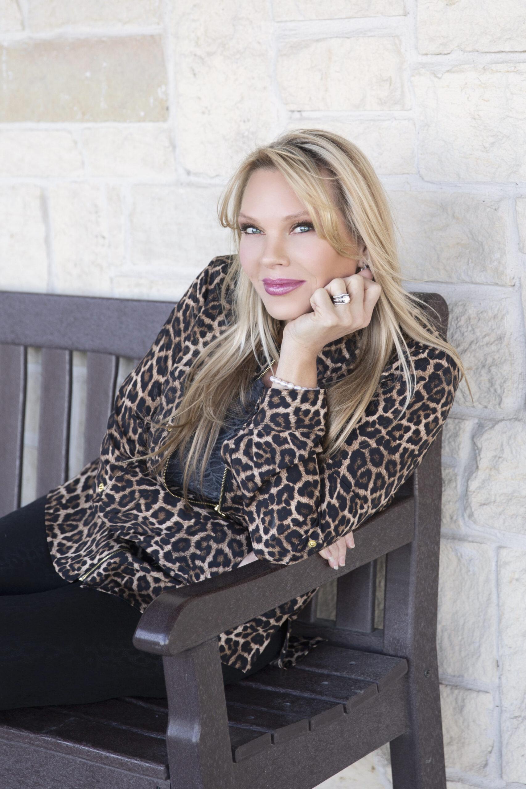 A woman in a leopard print jacket sitting on a bench with her hand on her cheek.